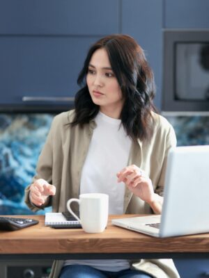 Focused young woman calculating budget while sitting with laptop and coffee at home.