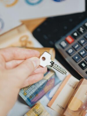 Hand holding key above Euro banknotes and calculator, symbolizing real estate investment.